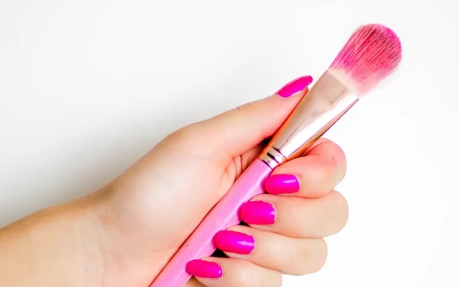 Main aux ongles roses tenant un pinceau de manucure, salon de Roanne