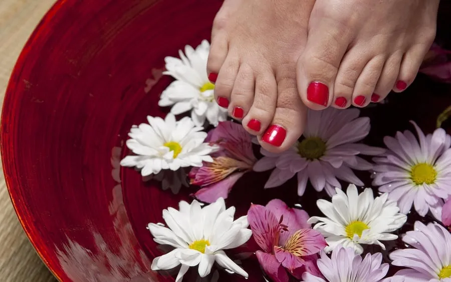 Pieds aux ongles vernis rouges dans un bain de pédicure fleuri, Roanne